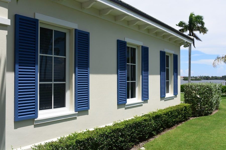 A Florida home with beige exterior and blue shutters, surrounded by a green lawn